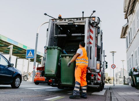 Ein Müllwerker bringt grüne Tonnen zum Müllwagen