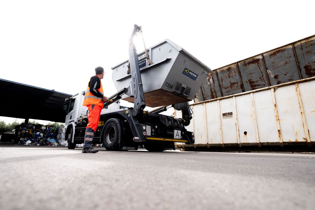 Ein Arbeiter in Warnkleidung entlädt einen Absetzmulden-Container mithilfe eines hydraulischen Arms von einem LKW.