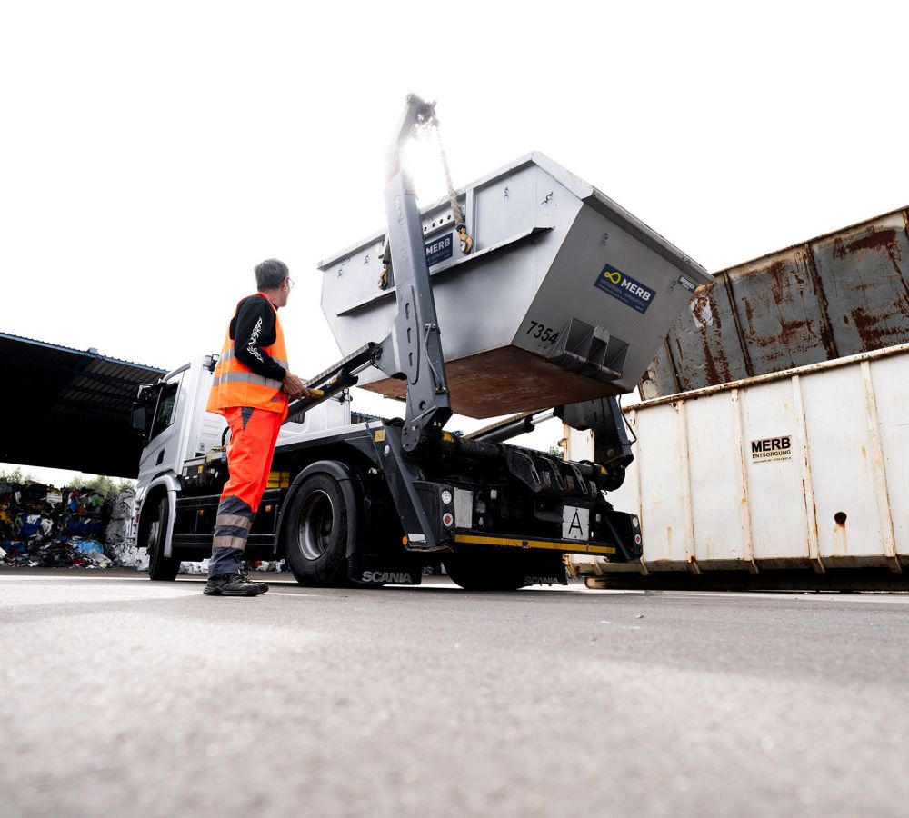 Ein Arbeiter in Warnkleidung entlädt einen Absetzmulden-Container mithilfe eines hydraulischen Arms von einem LKW.